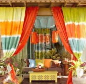 a colorful boho patio with bright curtains, pillows, lanterns, a neon coffee table and potted greenery