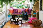 a colorful boho patio with a bright sofa and pillows, rattan chairs and an ottoman and potted blooms