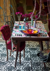 a colorful boho patio with a printed rug, a colorful tablecloth, bright blooms and vases