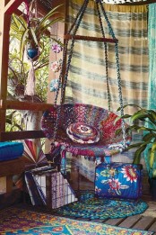 a super bright boho patio with a bold macrame hanging chair, pillows and cushions plus a macrame planter hanger