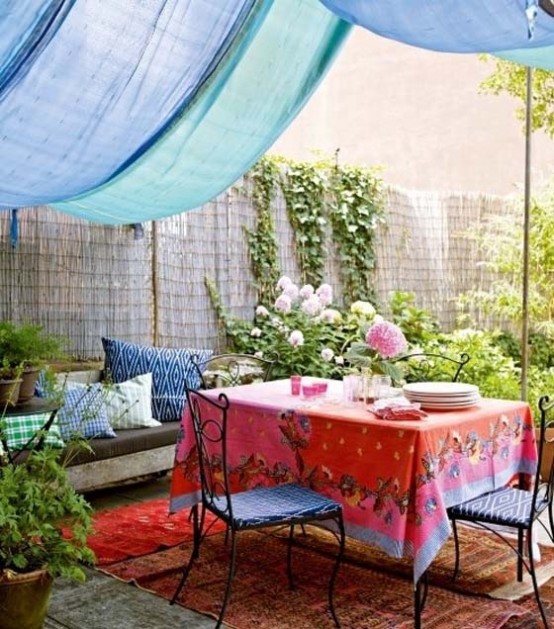 a colorful boho patio with a blue canopy, bright textiles and printed pillows, forged furniture