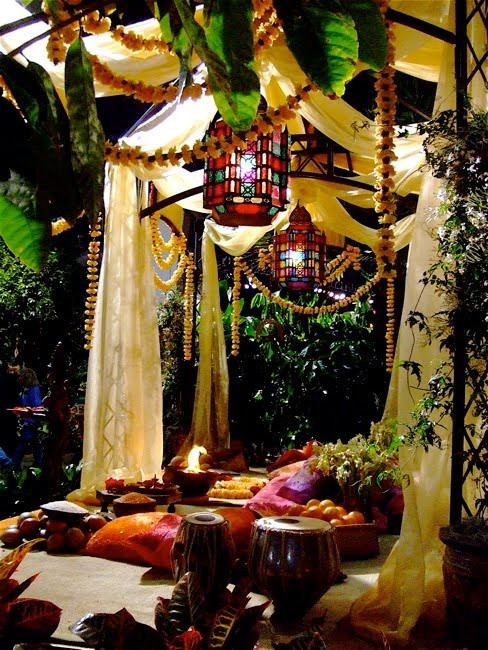 a colorful boho patio with bright pillows, cushions and fabric, floral garlands and drums plus Moroccan lanterns