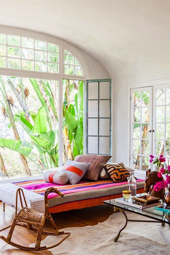 a refined colorful boho sunroom with a daybed with colorful pillows, bright blooms, a glass coffee table is very welcoming
