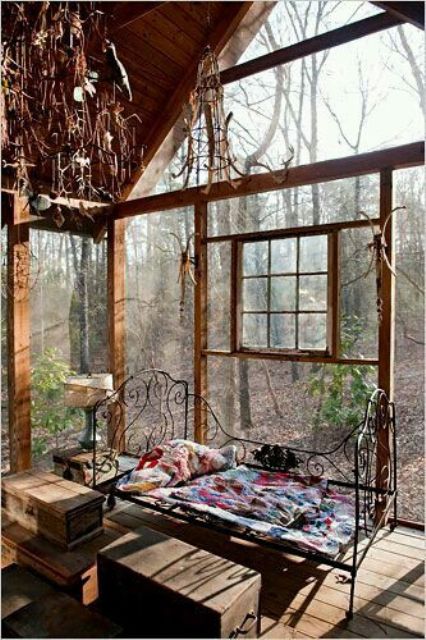 a shabby chic boho sunroom with a view of the forest, a forged bed, wooden chests and vintage chandeliers is a quirky space
