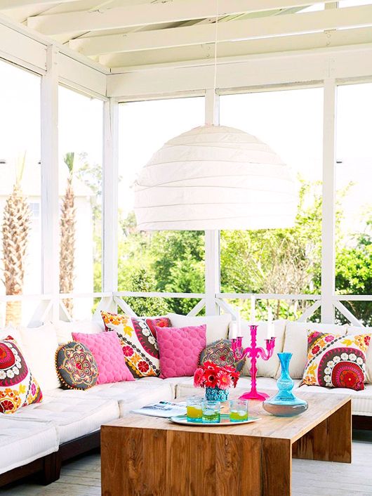 a bright boho sunroom with all white everything except for colorful and printed pillows and a rich stained table with colorful vases