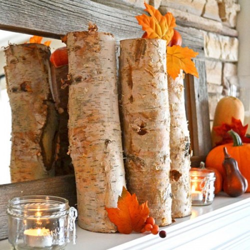 a fall mantel decorated with branches, candles in glass candleholders, bright pumpkins and leaves