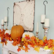 a chic fall mantel with bright fall leaves, orange and white pumpkins and candles in metallic candleholders