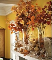 a rustic and modern fall mantel decorated with fall leaves in glass vases and pumpkins in large glass jars