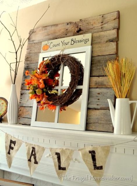 a rustic fall mantel with wheat, branches, a vine wreath with leaves and twigs, a burlap banner and a window