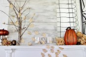 a cool fall mantel with some faux pumpkins, fake fall leaves, acorns, branches and dried hydrangeas