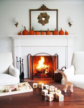 an elegant rustic mantel decorated with bright orange pumpkins, a wheat wreath hanging on a mirror