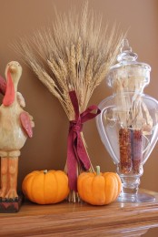 a colorful fall mantel with orange pumpkins, corn in a large glass jar, wheat and a fun chicken figurine