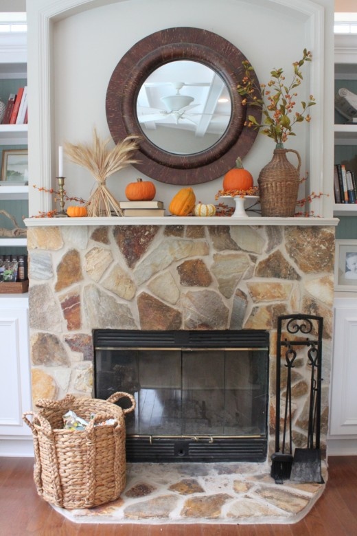 a chic fall mantel styled with wheat, berries, pumpkins and gourds, berry branches in a wicker vase plus a basket next to the fireplace