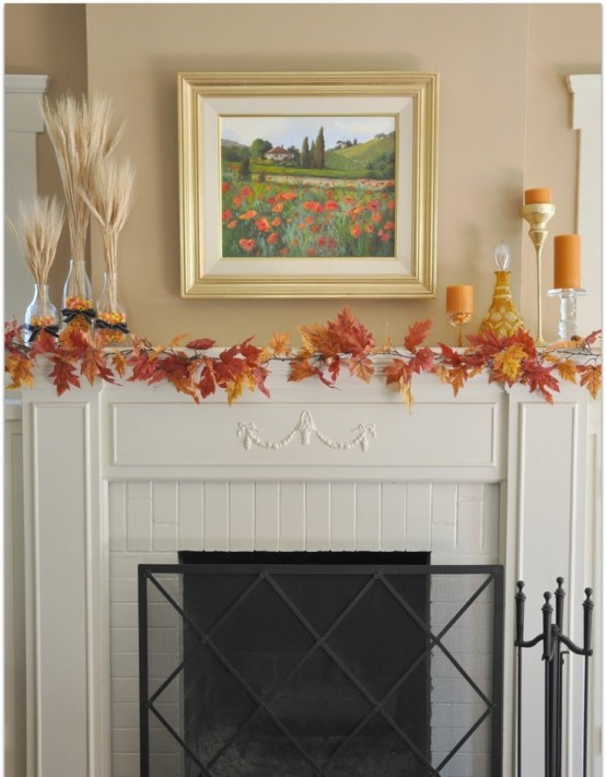 a simple fall mantel decorated with bright red fall leaves, wheat arrangements, candles in tall candle holders