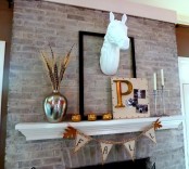 a fall mantel with a burlap banner, gilded pumpkins, a wheat arrangement, a sign and a faux animal head over it