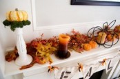 simple fall mantel decor with fake pumpkins, berries, candles in candleholders and a little pumpkin on a tall stand