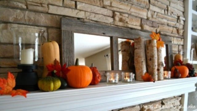 rustic mantel styling with candles, faux pumpkins, branches and a mirror in a vintage stained frame