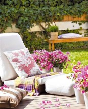 a bold floral deck with a low lounger, floral cushions and a bold blanket plus lots of blooms in buckets around