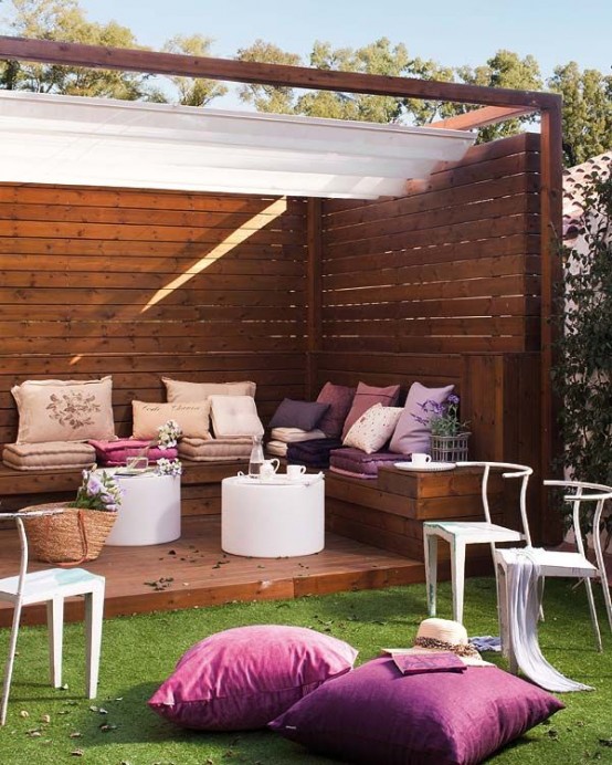 a lovely feminine terrace with stained wood around, with a built-in bench, pink, purple and pastel upholstery, white round coffee tables and white chairs, purple pillows