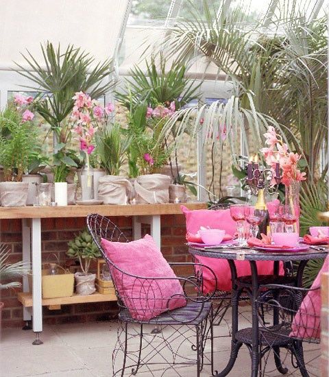 a pink tropical terrace with blakc forged furniture with pink upholstery and pillows, potted plants and blooms is a lovely space to be in