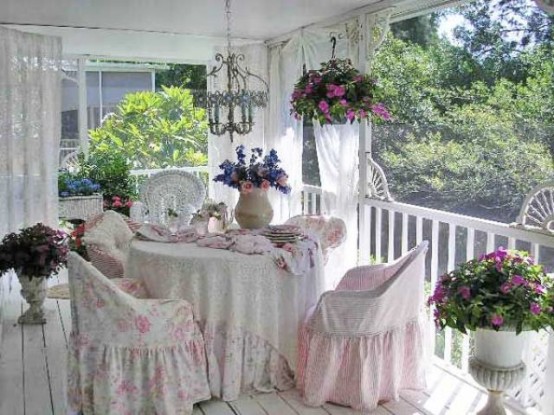 a refined vintage and shabby chic terrace with white furniture, woven chairs, pink floral upholstery and cushions and potted plants and blooms
