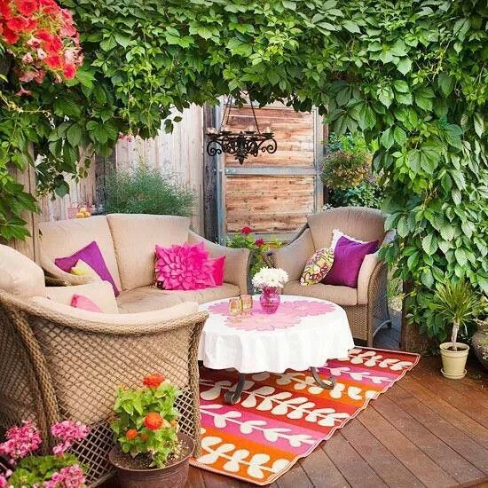 a bold terrace surrounded with greenery, with neutral furniture, with bright pillows and rugs, a table and bold potted blooms and plants