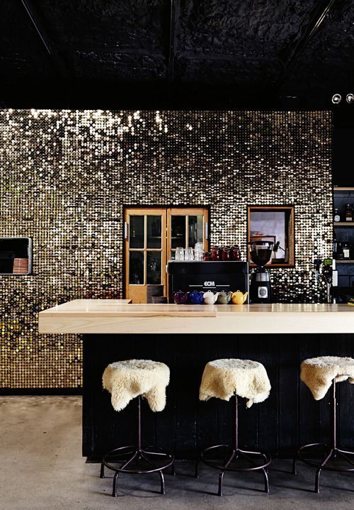 a dark glam kitchen with black furniture, a shiny tile backsplash, neutral stone countertops and faux fur stools
