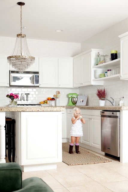 a neutral kitchen with white cabinetry, neutral stone countertops, a chic chandelier and a white tile backsplash