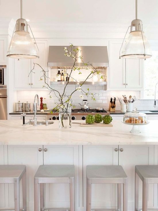 a modern neutral kitchen with touches of glam, with neutral furniture, white marble countertops, pendant lamps and shiny stools