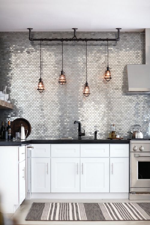 a modern kitchen with glam touches - white furniture, black countertops, a shiny silver tile backsplash and pendant lamps