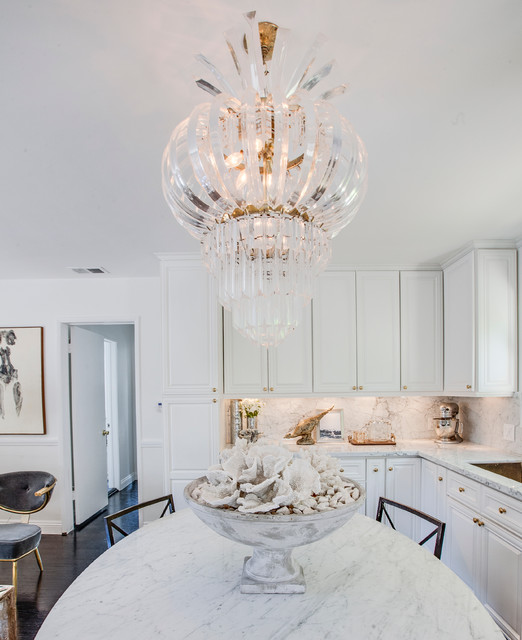a modern glam white kitchen with white marble countertops and a backspalsh plus a gorgeous glam chandelier over the table