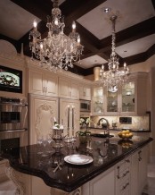 a vintage glam kitchen with white cabinetry, dark countertops, molding on the cabinets and crystal chandeliers