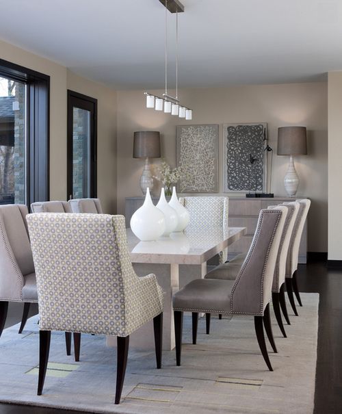 a sophsticated neutral dining room with a chic table with a stone tabletop, neutrla upholstered chairs, lovely lamps and some art