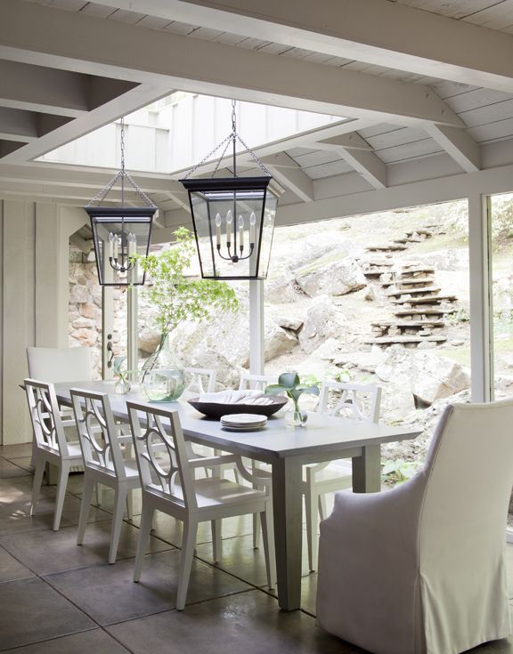 a neutral farmhouse dining room with a white dining set, a couple of metal pendant lamps and a beautiful view to the terrace