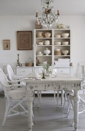 a vintage dining room done in neutrals, with a table, some white rattan chairs, a lovely storage unit and a crystal chandelier
