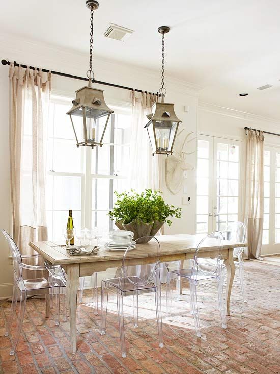 a neutral dining room with a wooden table and ghost chairs, pendant lamps, neutral textiles and some greenery
