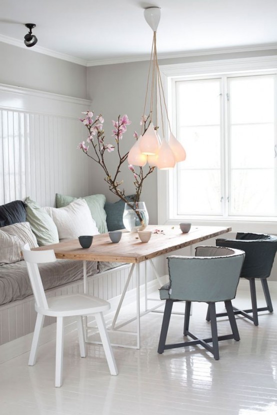 a neutral Scandinavian dining room with a paneled wall, pastel pillows, a cluster of pendant lamps and cool mismatching chairs