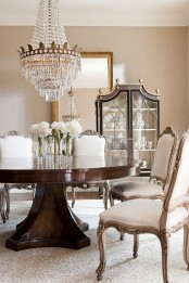 a refined glam dining room in neutral shades, with tan walls, a large floor mirror, a round dark stained table and vintage chairs plus a statement chandelier