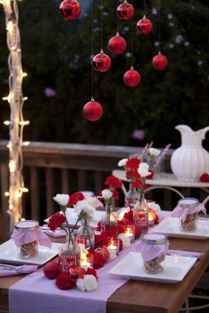 a red and white Christmas table setting with ornaments hanging over the table, red and white blooms in bottles and matching ornaments on the table
