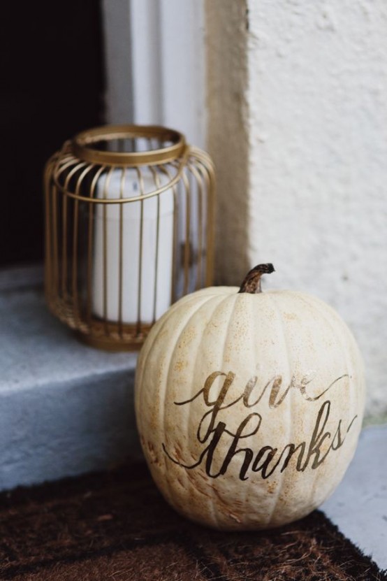 a pillar candle in a candle holder and a neutral pumpkin with letters compsoe a cool decoration for outdoors