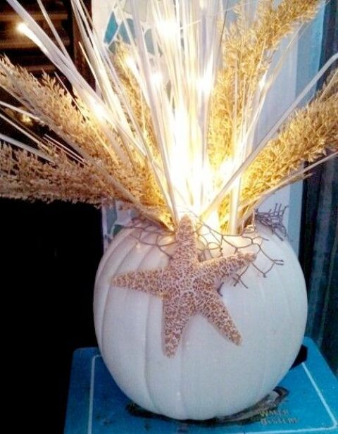 a white pumpkin with starfish, wheat and pampas grass plus lights is a bold beach Thanksgiving centerpiece or decoration