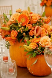 bright orange pumpkins with bright orange blooms, greenery and berries for Thanksgiving centerpieces or decorations