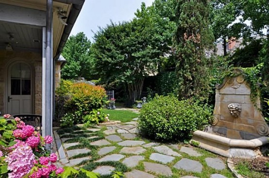 a large townhouse garden with stones, grass, a fountain, planted greenery and bright blooms