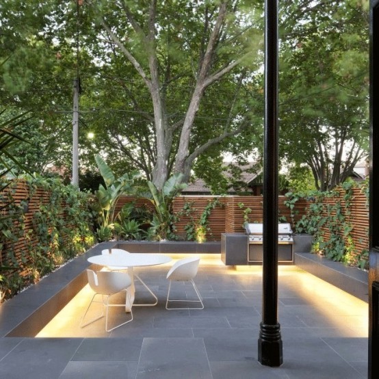 a minimalist townhouse garden done with stone tiles, additional lights, benches and living walls