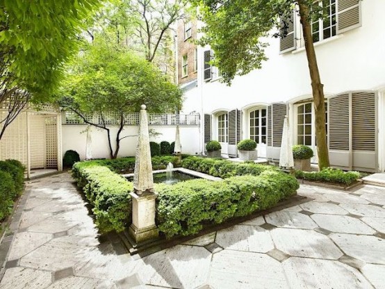 an elegant garden space with large tiles, a fountain with planted greenery lining up the fountain and the whole space