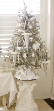 a silver Christmas tree done with white and silver ornaments, silver cones with decorations looks very vintage and serene