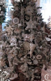 a snowy Christmas tree with white and silver ornaments of glass and paper, with shiny snowflakes and garlands