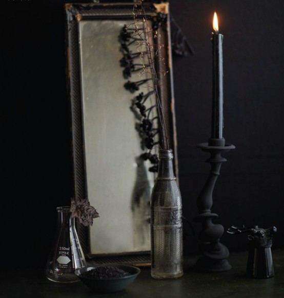 delicate vintage Halloween decor with a mirror, a test tub as a vase, bottle with branches and a black candleholder with a black candle