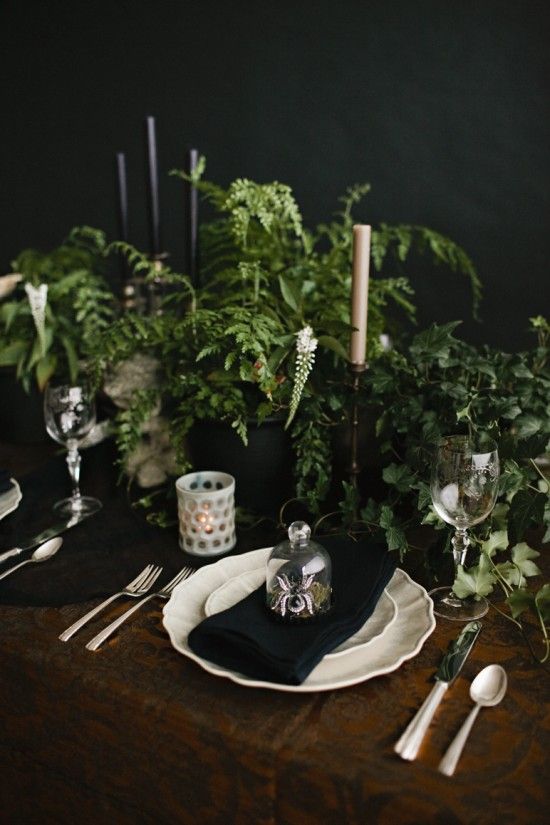 a fresh vintage Halloween tablescape with lots of greenery, black and white candles, white candleholders, porcelain and metallic cutlery is cool