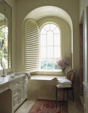 a creamy and beige vintage-inspired bathroom with an arched window and a chic vanity